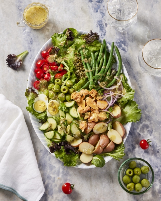 Fresh green salad with cucumber, white beans, and 80 Acres Farms dressing on white marble surface