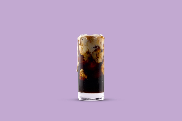 Tall glass of iced coffee with Horizon Organic creamer swirling inside against a purple studio background.