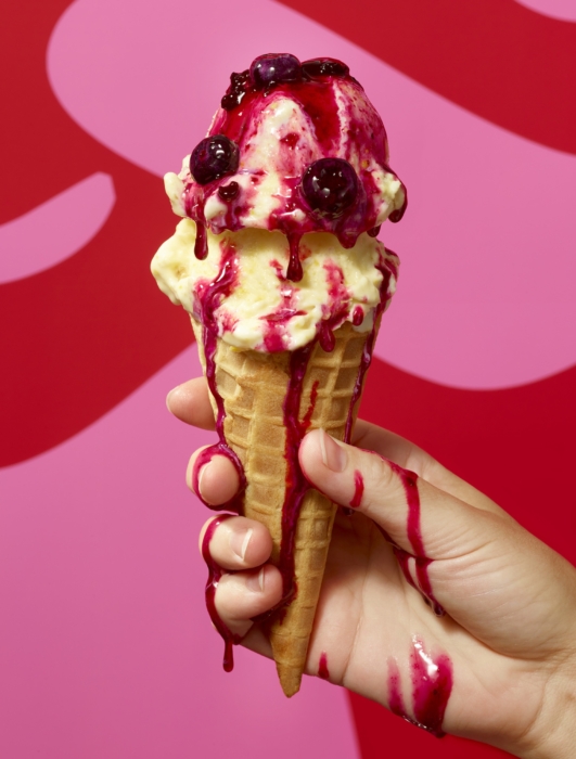 Ice cream cone with berry sauce held in hand — dessert food photography by OMS Photo