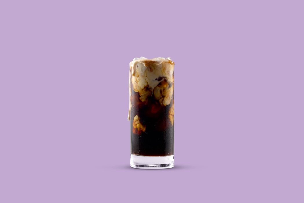 Tall glass of iced coffee with Horizon Organic creamer swirling inside against a purple studio background.