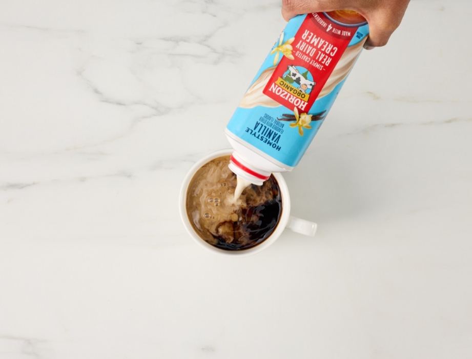 Top-down view of Horizon Organic coffee creamer pouring into hot coffee in a white mug.