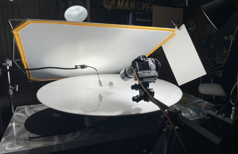 Commercial photography studio setup with camera and lighting equipment photographing a football helmet on a reflective surface