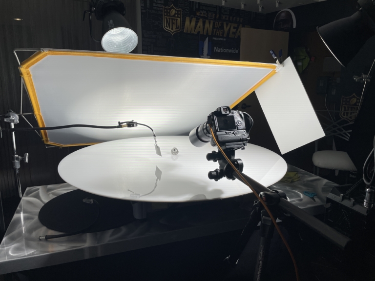 Commercial photography studio setup with camera and lighting equipment photographing a football helmet on a reflective surface
