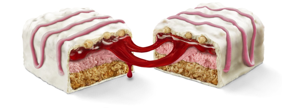 Cross-section of white-frosted protein bar with pink berry filling and red jam drizzle split in half