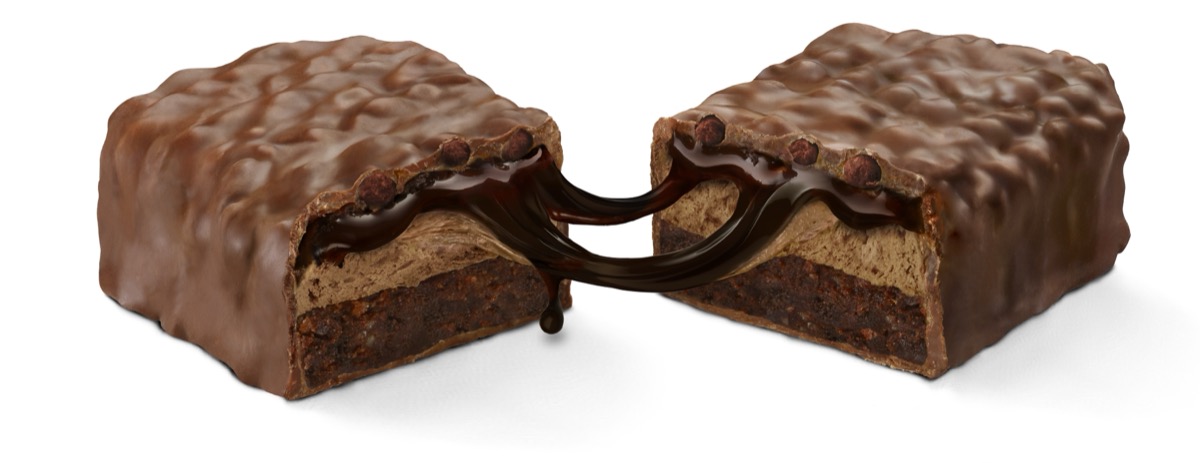 Cross-section of chocolate-covered candy bar split in half showing gooey caramel and nougat layers
