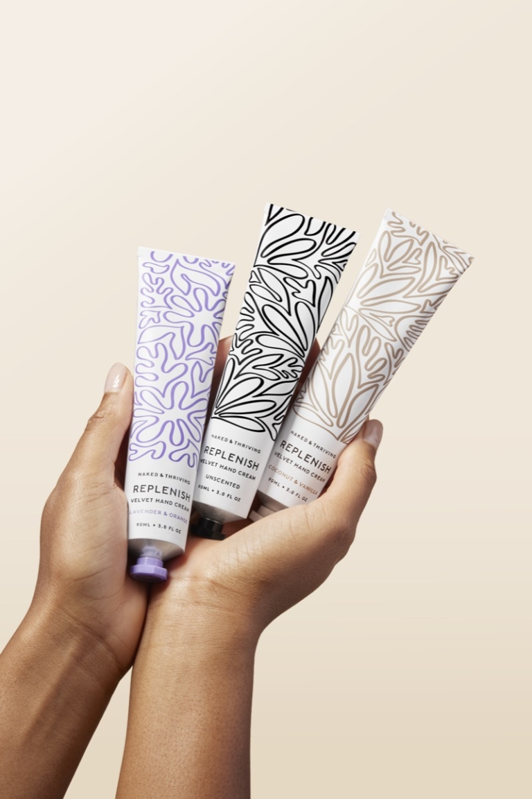 Hand holding Naked & Thriving hand cream tubes on soft pink background