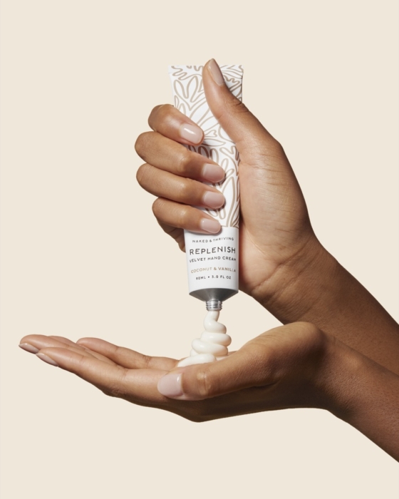 Hand holding Naked & Thriving serum bottle dispensing product on warm neutral background