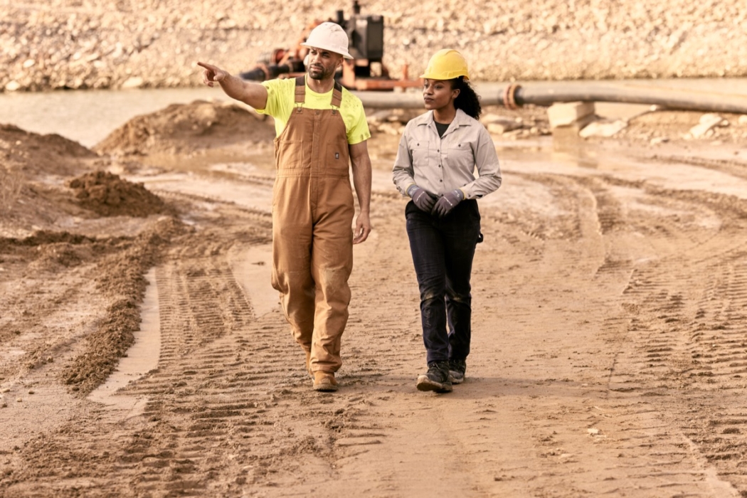 Two workers walking through a construction site wearing safety gear and workwear