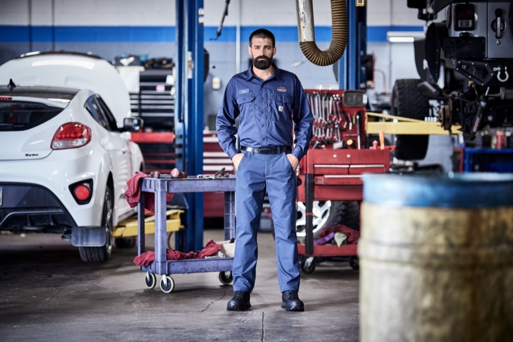 Male mechanic in navy blue uniform standing confidently in an automotive repair shop with vehicles in background