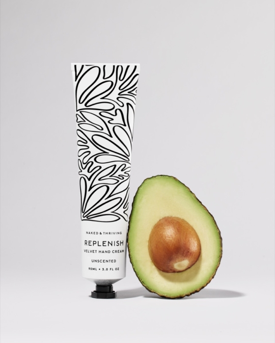 Naked & Thriving hand cream tube with fresh avocado on warm peach background