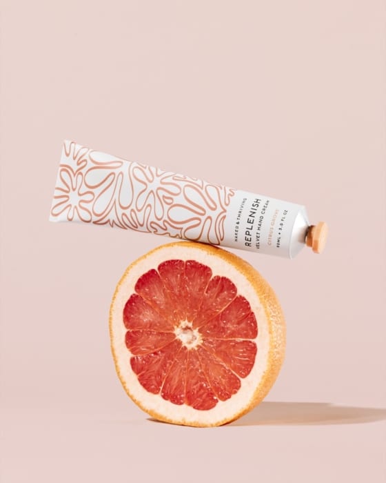 Naked & Thriving hand cream tube with fresh grapefruit on soft pink background