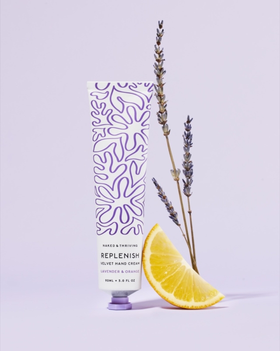 Naked & Thriving Replenish hand cream tube with fresh lavender sprigs and lemon slice on soft lavender background