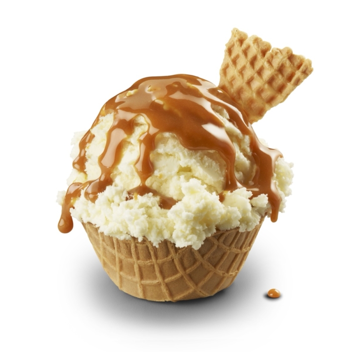 Scoop of vanilla ice cream in waffle cone bowl drizzled with caramel sauce and waffle cone piece garnish