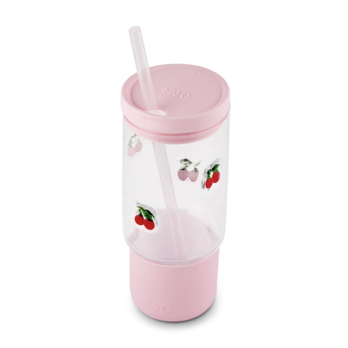 Clear Ello glass tumbler with cherry charm decorations, pink silicone sleeve, lid, and angled straw on white background
