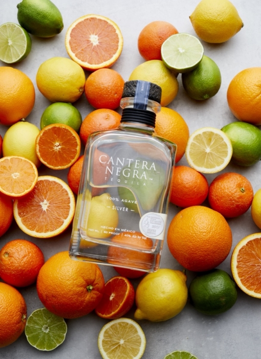 Cantera Negra Silver Tequila bottle surrounded by oranges, lemons, and limes in overhead flat lay photography