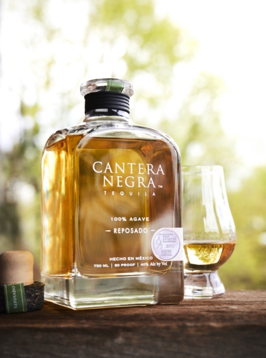 Cantera Negra Reposado Tequila bottle with silver medal award beside filled tasting glass in soft outdoor sunlight