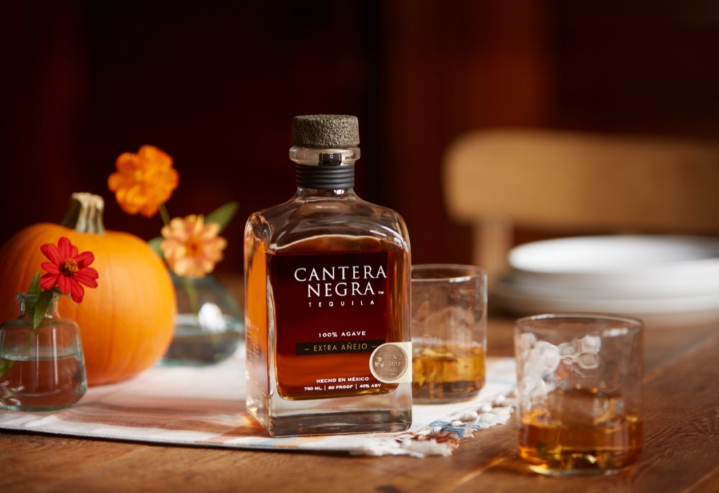 Cantera Negra Extra Anejo Tequila bottle with textured cork top styled on fall tablescape with pumpkins, flowers, and whiskey glasses