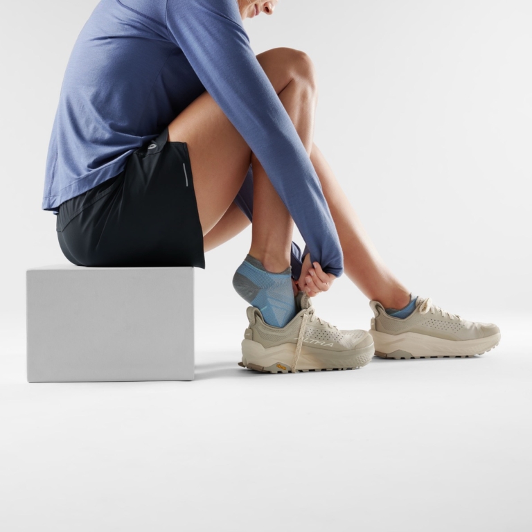 Person sitting on a cube wearing casual shoes and adjusting laces in a studio setting