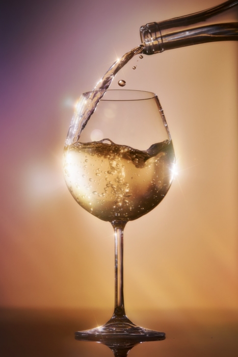 Sparkling white wine being poured into a glass with bubbles and splash captured in high-speed liquid photography
