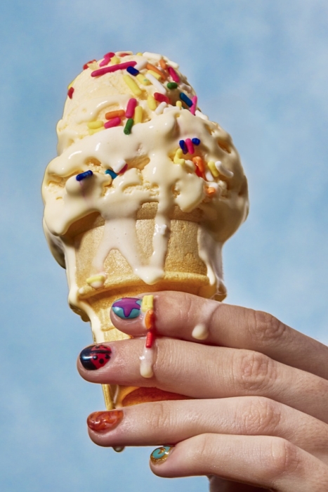 Hand with colorful nail art holding a melting ice cream cone with sprinkles