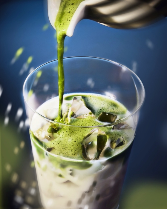 Green matcha being poured into iced milk creating a layered matcha latte in a glass