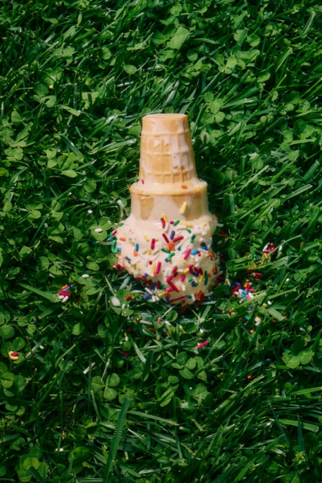 Melting vanilla ice cream cone with sprinkles placed upside down on green grass