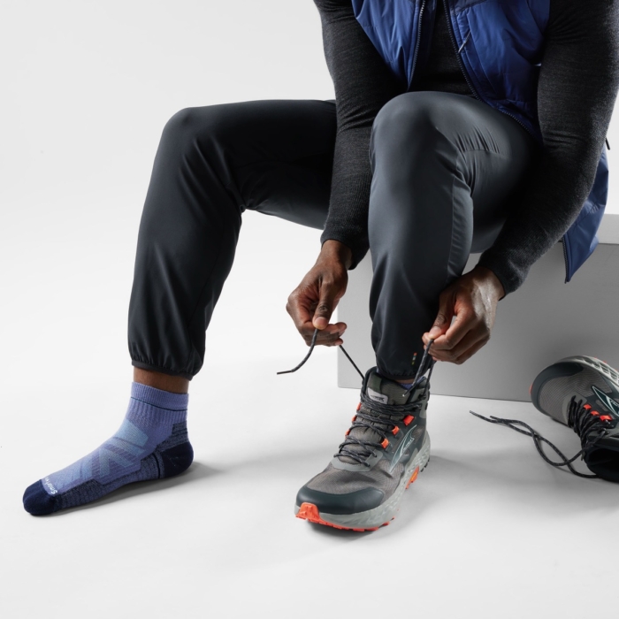 Person lacing up hiking boot with blue performance sock visible, on-model outdoor footwear and sock product photography by OMS Photo