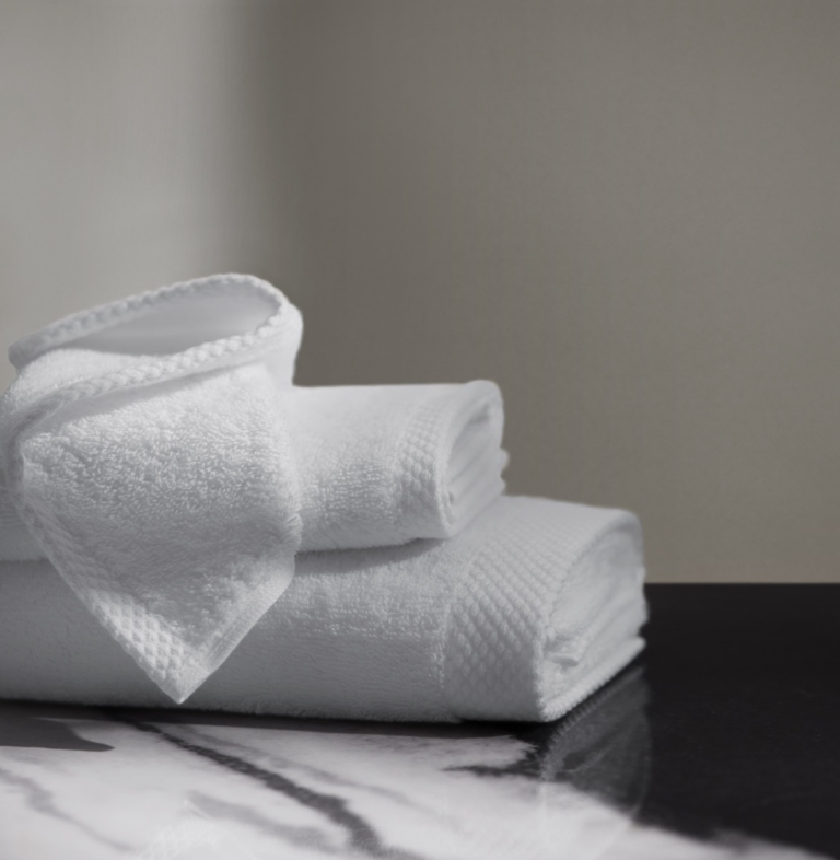 Rolled white waffle-weave and terry towels stacked on dark marble with negative space background