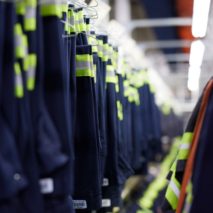 Long row of navy blue and yellow high-visibility work jackets hanging on a rack in an industrial facility