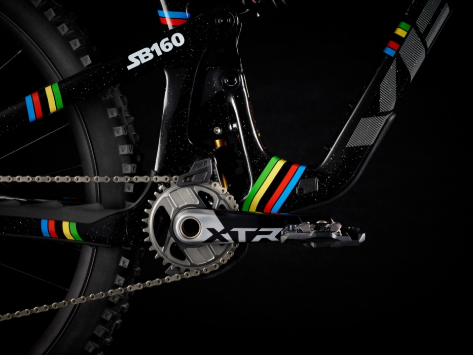 Studio macro of Shimano XTR crankset and chainring on Yeti SB160 Richie Rude World Champion mountain bike, showing SB160 frame badge, UCI rainbow stripe chainstay accents, and Schwalbe knobby rear tire in black studio setting