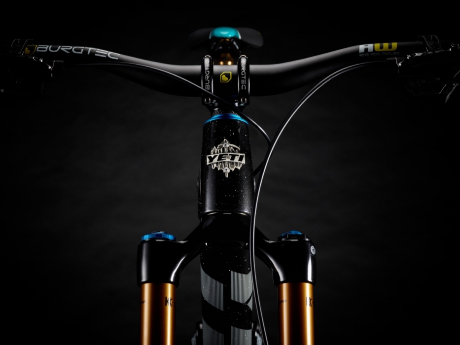 Front-facing studio portrait of Yeti SB160 mountain bike showing Burgtec carbon handlebar with RW grip ends, Yeti head tube badge with Abominable Snowman logo, teal headset cap, and Fox 40 Factory fork with bronze stanchions in dramatic dark studio lighting