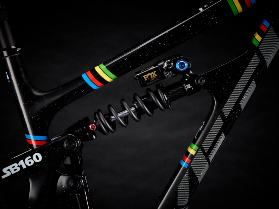 Yeti SB160 full-suspension mountain bike frame detail showing FOX LiveValve coilover rear shock with blue adjuster, SB160 downtube badge, and UCI World Champion rainbow stripe wraps on black carbon with galaxy speckle finish