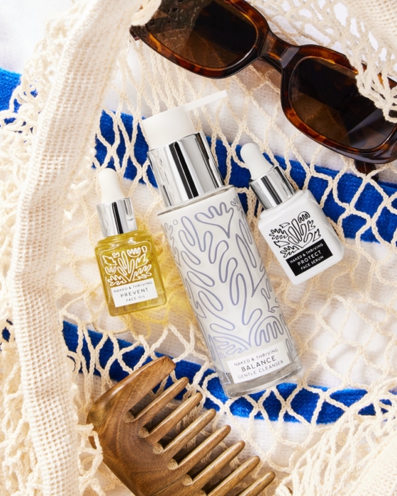 Naked and Thriving Prevent Face Oil, Balance Cleanser, and Protect Face Serum styled on woven beach bag with tortoiseshell sunglasses and wooden comb