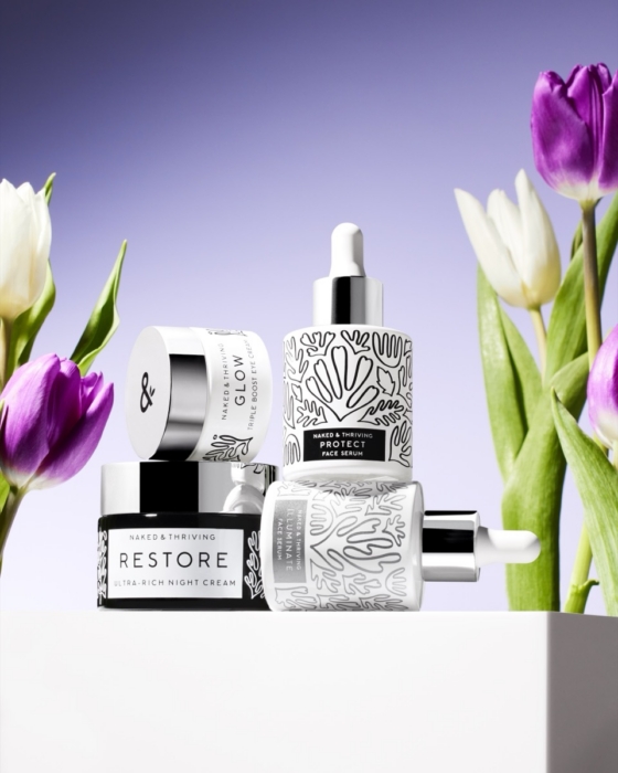 Naked & Thriving Restore skincare collection bottles with purple tulips on soft lavender background