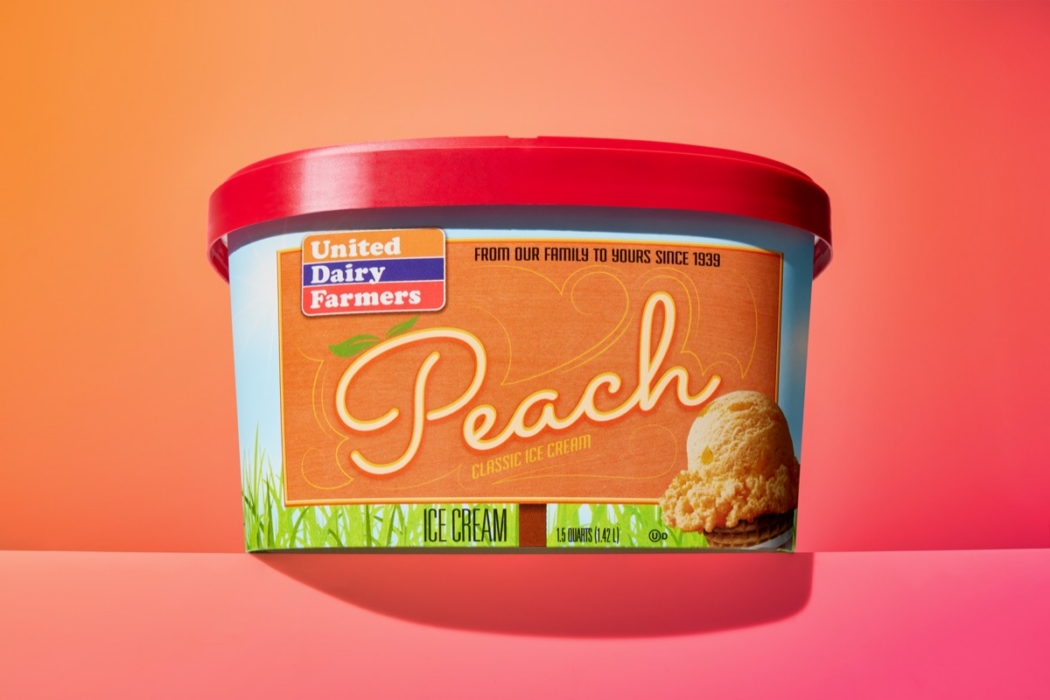 United Dairy Farmers Peach Classic Ice Cream 1.5 quart container with red lid on colorful orange to pink gradient background