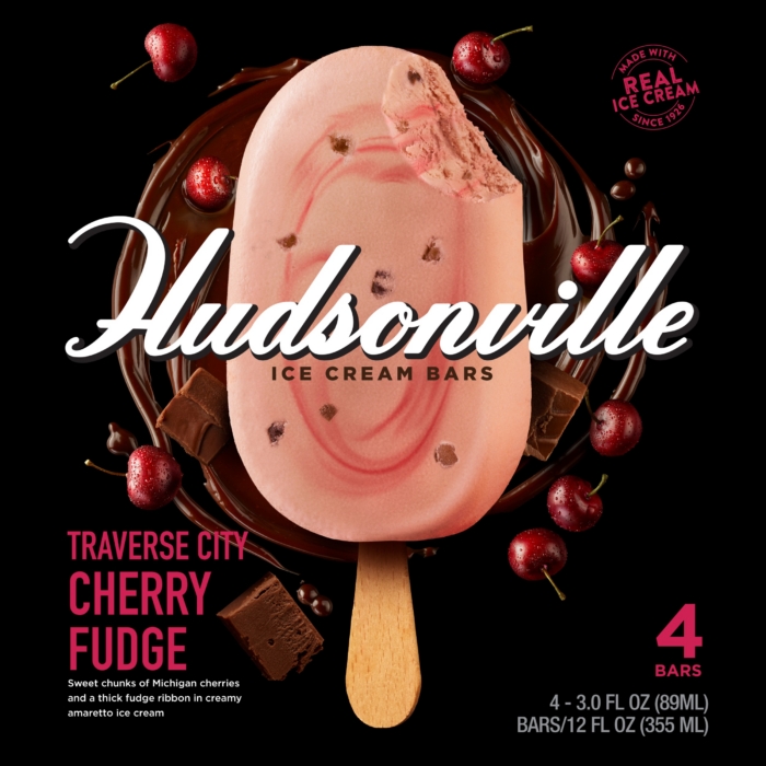 Hudsonville Traverse City Cherry Fudge ice cream bar box with chocolate drizzle, fresh cherries, and fudge chunks on black background