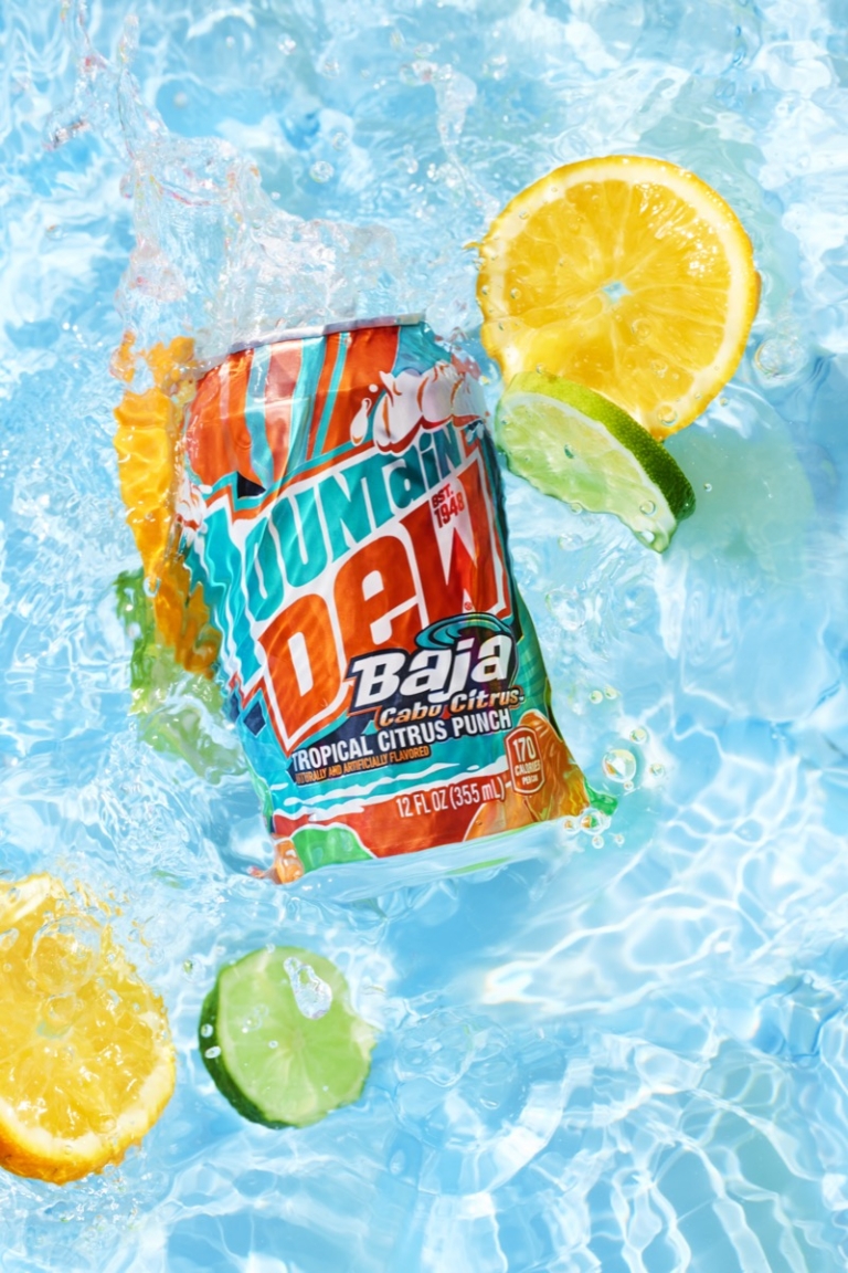 Can of Mountain Dew Baja Blast tropical citrus punch submerged in splashing ice water surrounded by lemon and lime slices