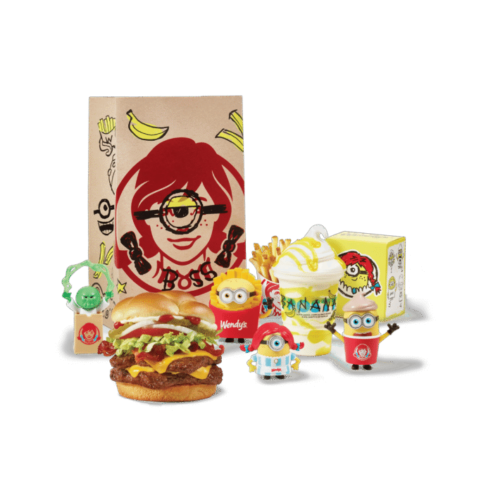 Wendy's Minions and Monsters meal spread featuring a burger, fries, banana Frosty, and four collectible toy figures beside a branded bag