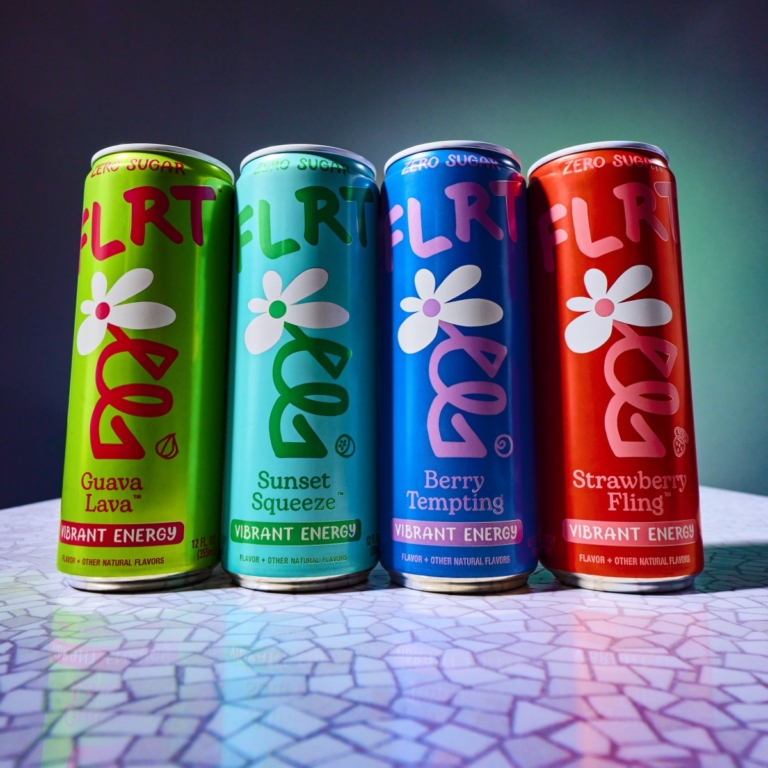 Four FLRT zero sugar energy drink cans in Guava Lava, Sunset Squeeze, Berry Tempting, and Strawberry Fling flavors lined up on a reflective tiled surface
