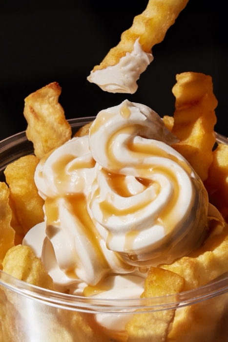 Cup of caramel whipped cream topped fries sitting on a checkered floor beside guest check tickets