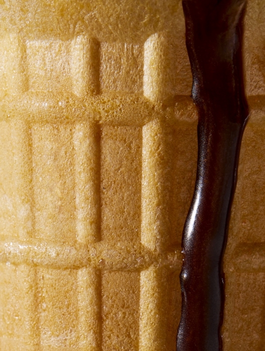 Extreme close-up of a textured waffle cone with a thin stream of chocolate sauce dripping down its ridged surface