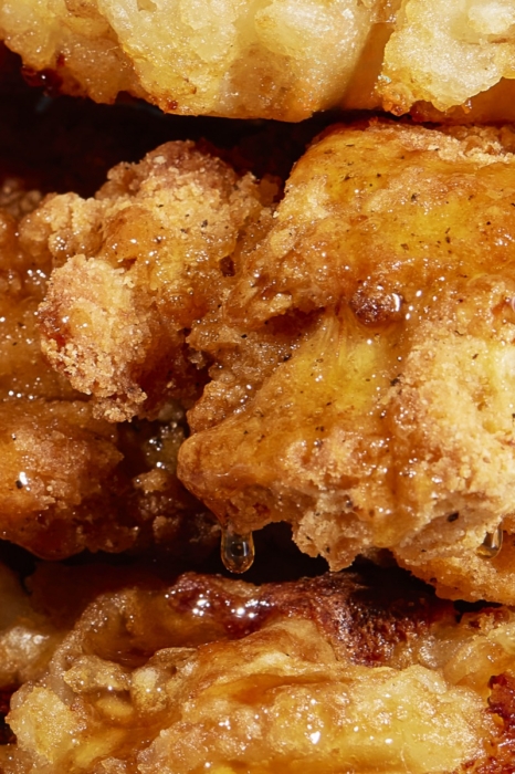 Extreme close-up of crispy fried chicken bites glazed with honey and dripping sauce, stacked together