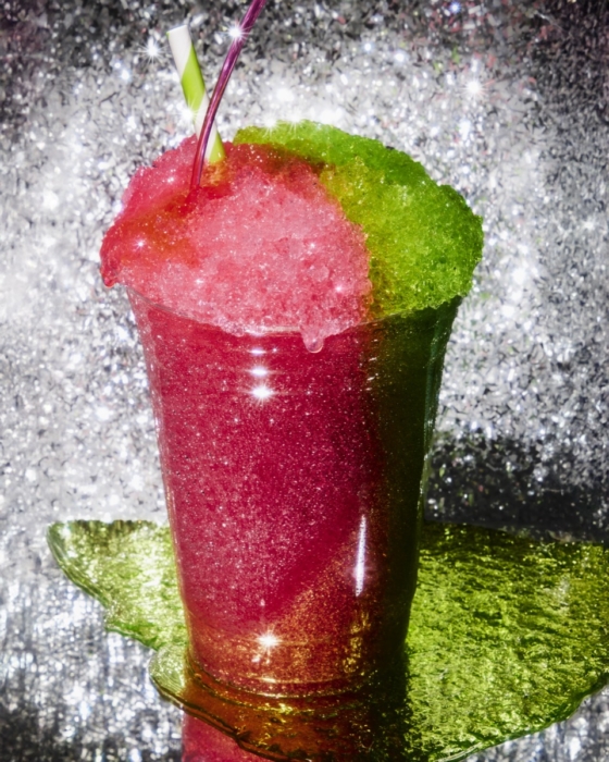 Red and green layered frozen slushie drink with striped straws in a clear cup on a glittery silver and green background