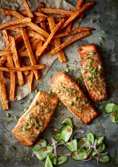 Overhead shot of seasoned salmon fillets topped with crispy shallots and edamame beside sweet potato fries and a cucumber salad