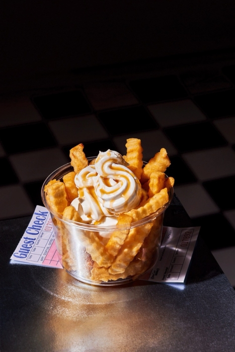 Close-up of crinkle cut fries topped with swirled whipped cream and caramel sauce, with a cream-dipped fry hovering above the cup