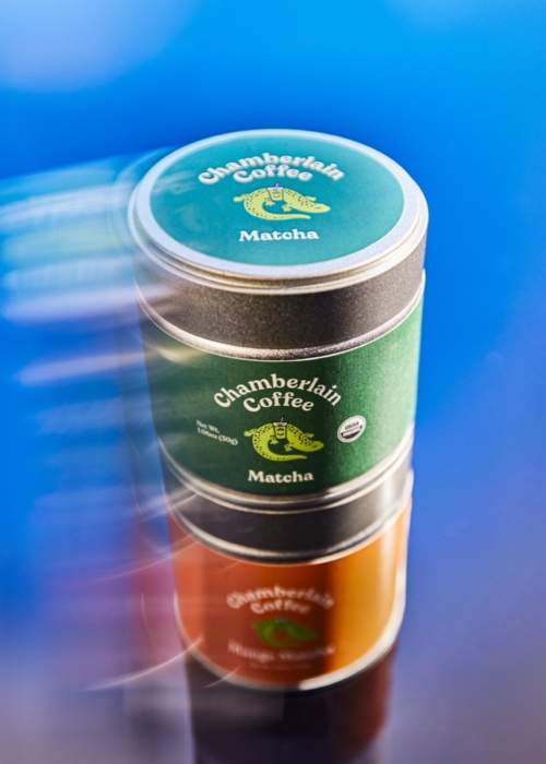 Three stacked tins of Chamberlain Coffee Matcha and Mango Matcha powder with motion blur background in blue tones