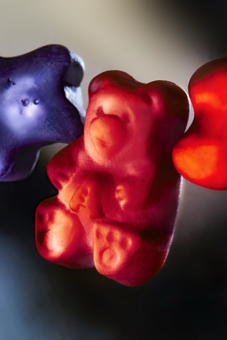 Extreme close-up of purple, red, and orange gummy bears backlit against a dark gradient background showing translucent candy texture
