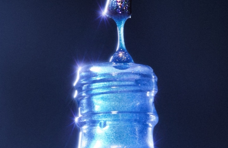 Glittery blue nail polish brush dripping a bead of polish back into an open glass bottle against a dark background