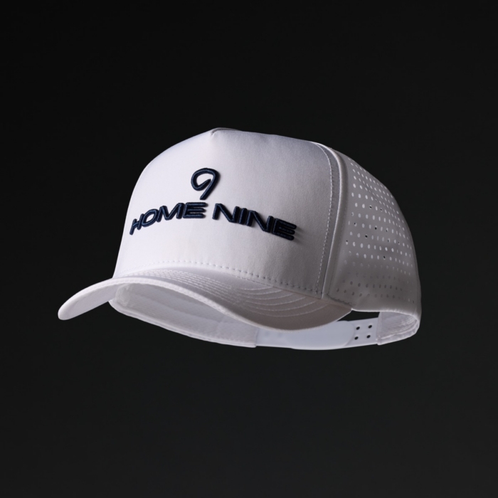 White performance trucker hat with Home Nine embroidered in navy on the front panel and perforated side paneling