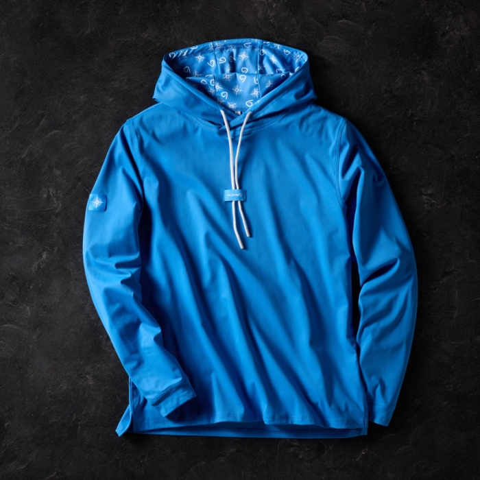 Bright blue hooded long sleeve shirt with white drawstrings and patterned hood lining, laid flat on dark stone background